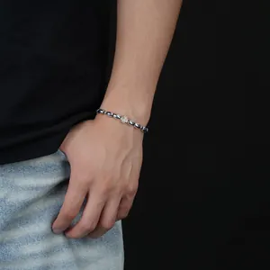 Nahaufnahme eines silbernen Kaffeebohnen-Kreuz-Perlenarmbands an einem Handgelenk.