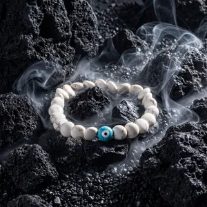 Close-up of white bead bracelet with blue evil eye charm on black volcanic rocks