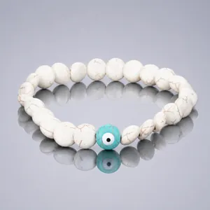Close-up of white marbled beaded bracelet with a blue Evil Eye centerpiece on reflective surface
