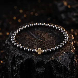 Nahaufnahme eines stilvollen Hämatit-Perlenarmbands mit goldenem Kreuz auf dunklem Fels
