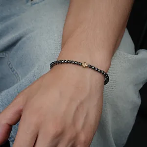 Nahaufnahme eines Herrenarmbands mit dunklen Perlen und goldenem Kreuz am Handgelenk.