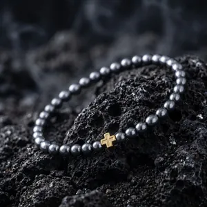 Detailreiche Makroaufnahme eines schwarzen Metallperlenarmbands mit goldenem Kreuz