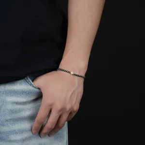 Detailansicht eines minimalistischen schwarzen Perlenarmbands mit goldenem Kreuz für Herren.