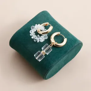 Detailed view of asymmetrical gold hoop earrings with clear crystals on green velvet