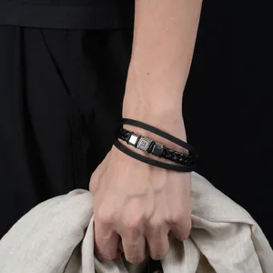 Macro shot of a retro black braided leather bracelet with patterned metal clasp on a wrist.