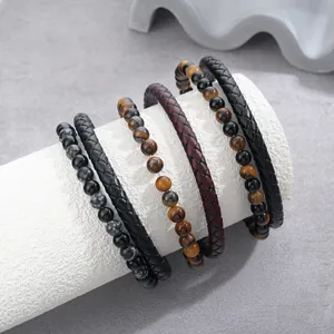 Close-up view of stacked braided leather and tiger eye stone bead bracelets on a white stand
