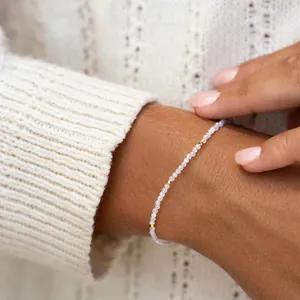 Detailopname van een delicate kralenarmband met maansteenkralen en gouden tussenstukjes op een pols.