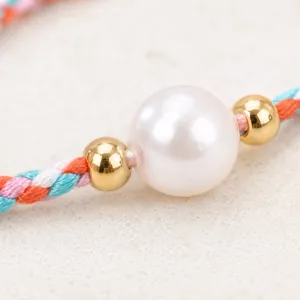 Detail view of large white pearl and gold beads on a colorful braided cord bracelet