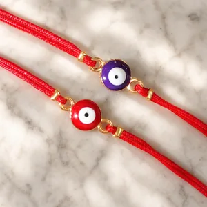 Close-up detail of handmade red cord bracelets featuring colorful evil eye charms