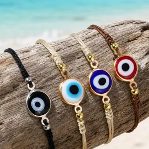 Handmade evil eye braided bracelets displayed on driftwood with a beach background