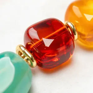 Close-up of a colorful resin barrel bead bracelet with red, orange and teal translucent beads.
