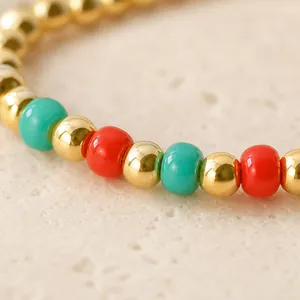 Festive Christmas beaded bracelet with gold, red, and teal accents on a stone surface.