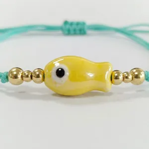 Bracelet tissé vert menthe avec poisson en céramique jaune et billes dorées.