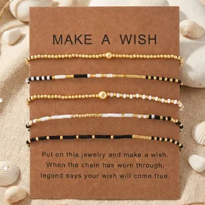 Set of 5 handmade wish-themed seed bead bracelets in black white and gold on a card