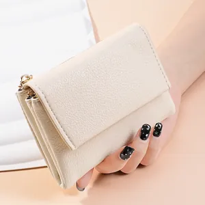 Detail showing a cream-colored pebble-grain mini wallet with gold zipper held by a hand