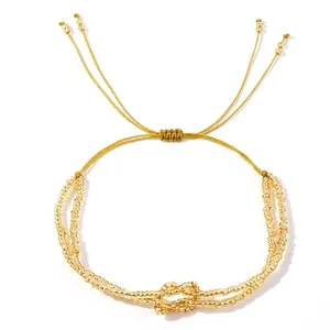 Gold beaded bracelet with central knot design and adjustable cord on white background.