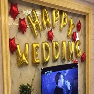 Gros plan de ballons en aluminium HAPPY WEDDING dorés et d'étoiles rouges sur un mur marbré
