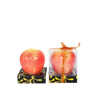 Velas de Navidad realistas con forma de manzana en caja de regalo sobre fondo blanco puro.