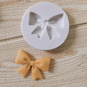 Detail of circular bow-shaped silicone mold with yellow fondant bow on textured wood.