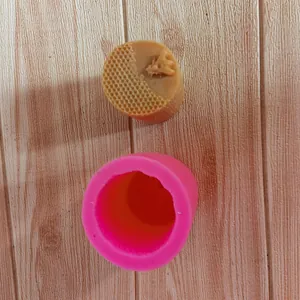 Close-up detail of a pink silicone honeycomb mold and a brown wax cast on wood background.