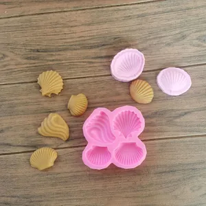 Stampi in silicone rosa a forma di conchiglia con cioccolatini su fondo di legno.