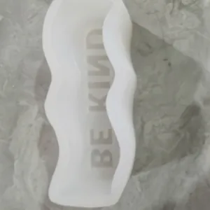 Macro detail view of wavy silicone mold interior with reversed BE KIND phrase engraving