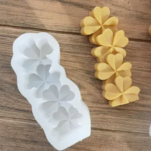 Moule trèfle en silicone blanc avec des pièces de cire jaune sur une surface en bois