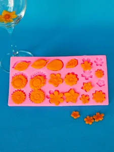 Pink silicone mold with various orange fondant flowers and leaves on blue background.