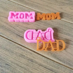 Detalle de moldes de silicona MOM y DAD con productos terminados de resina sobre madera.