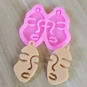 Close-up of pink abstract face silicone mold with two finished beige resin pendant samples