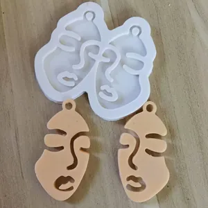 Detailed view of an abstract face silicone mold and two finished beige resin keychains