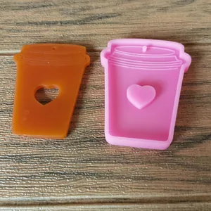 Macro view showing a pink coffee cup silicone mold next to an orange heart resin piece.