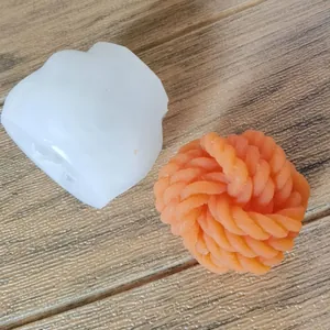 Detail of white silicone mold and orange yarn ball candle on wooden surface