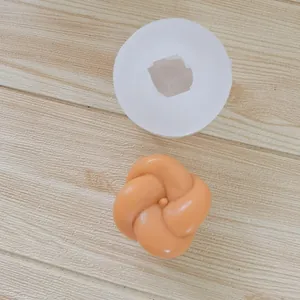 Detailed view of white silicone knot ball mold and orange finished candle on wood