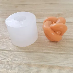 Detailed view of silicone knot ball candle mold next to finished orange wax cast