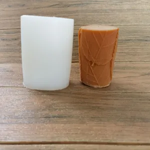 Cylindrical silicone mold with leaf pattern next to a finished brown wax candle
