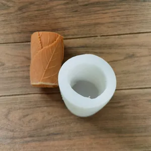 Detailed view of white cylindrical silicone mold and finished leaf-patterned candle