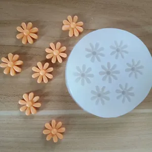 Detail of white silicone daisy flower mold with finished orange fondant samples on wood