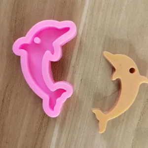 Detaillierte Ansicht der rosa Delfin-Silikonform und des fertigen Harzanhängers auf Holz