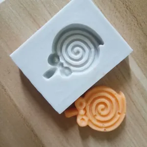 Detalle macro de un molde de silicona para piruletas y una artesanía naranja en espiral.