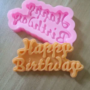 Dettaglio macro di uno stampo Happy Birthday in silicone rosa e il suo output arancione
