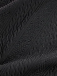Close-up of black jacquard knit fabric showing intricate cable and diamond patterns