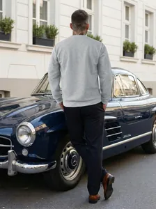 Back view of a man wearing a grey jacquard sweatshirt leaning on a classic blue car.