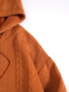 Détail d'un sweat à capuche orange rouille avec motif jacquard torsadé et texture
