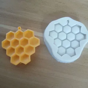 Close-up of a white honeycomb silicone mold alongside a yellow hexagonal resin piece
