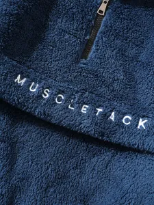 Close-up view of navy blue sherpa fleece texture with white MUSCLETACK letter embroidery