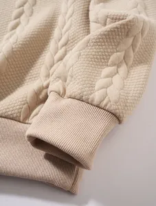 Gros plan d'un sweat à capuche en maille beige avec motif torsadé et poignets côtelés.