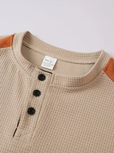 Detailaufnahme von Waffelstrickstoff und Kragenknöpfen an khakifarbenem Herren-Henley-Shirt