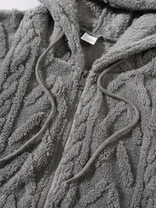 Gedetailleerde close-up van een grijze pluizige hoodie met kabelgebreide textuur en ritssluiting