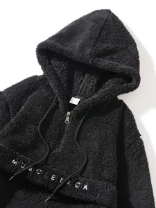 Detail view of black plush hoodie with MUSCLE TACK embroidery and drawstring hood.
